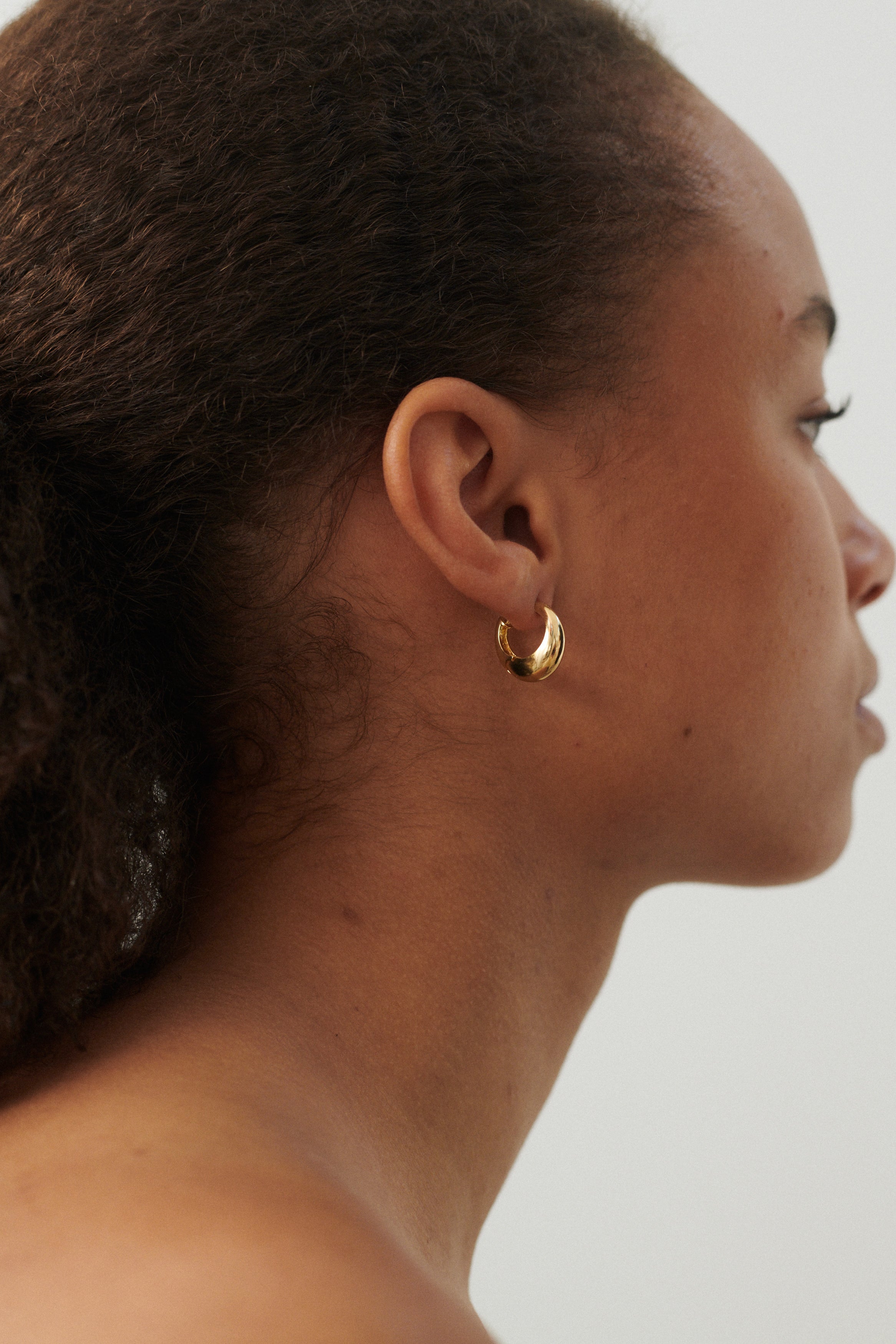 Stylisches Model trägt Mini Globe Huggies Ohrringe in Gold, Alltagsschmuck mit zeitlosem Design