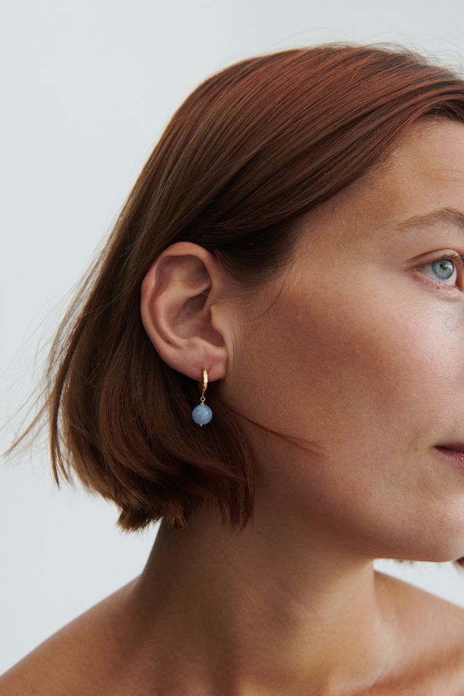 Model mit seitlichem Blick trägt goldene Blue Sky Ohrringe von Pernille Corydon mit schimmerndem blauem Achat – eleganter Sommerlook