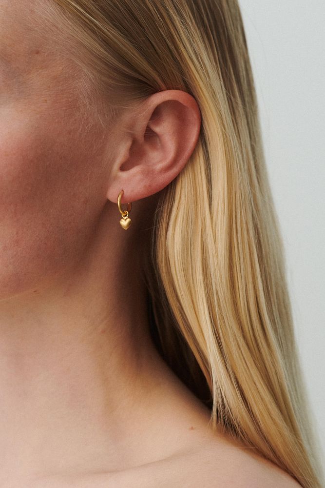 Model trägt goldene Heart Huggies Ohrringe mit Herz-Design von Pernille Corydon